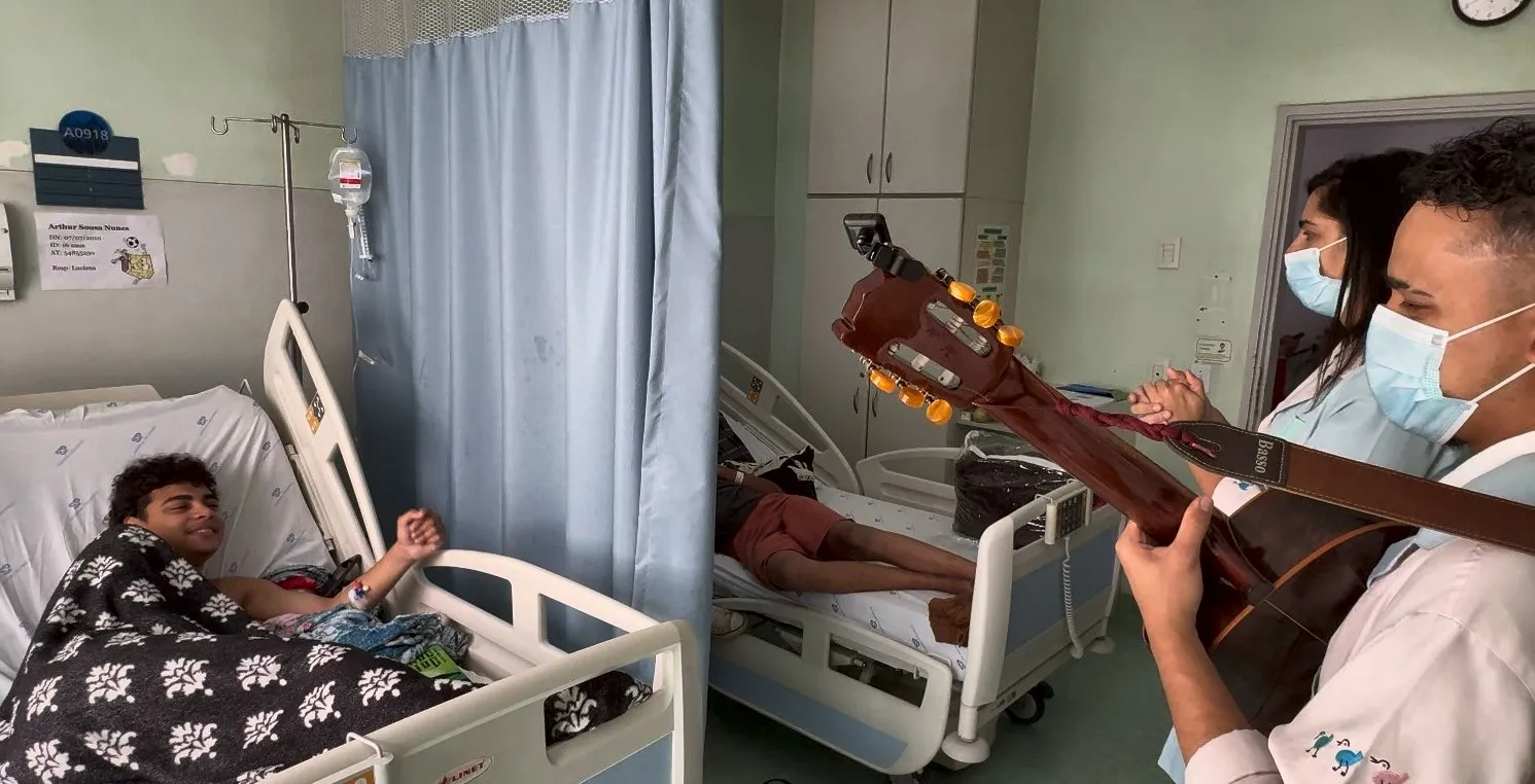 Artista toca violão para um adolescente no leito