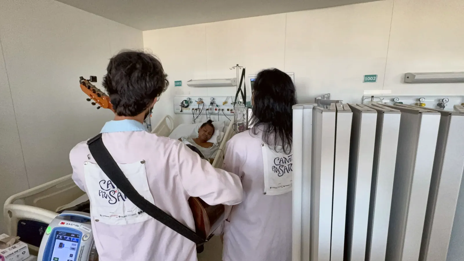 Dupla de artistas toca para uma paciente deitada, num quarto do ICESP