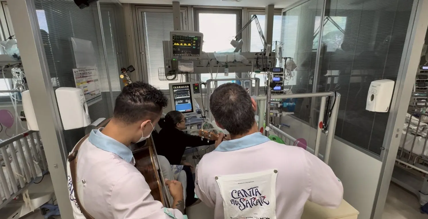 Dupla de jaleco toca para uma paciente entre os monitores de uma UTI